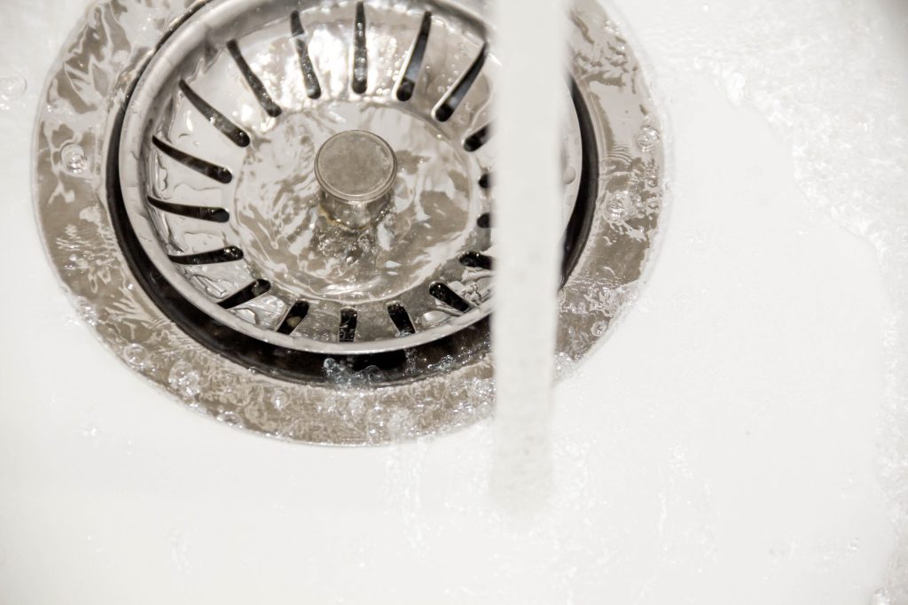 Close-up of a kitchen sink drain with water flowing smoothly, indicating a clean and clear drain after professional cleaning.