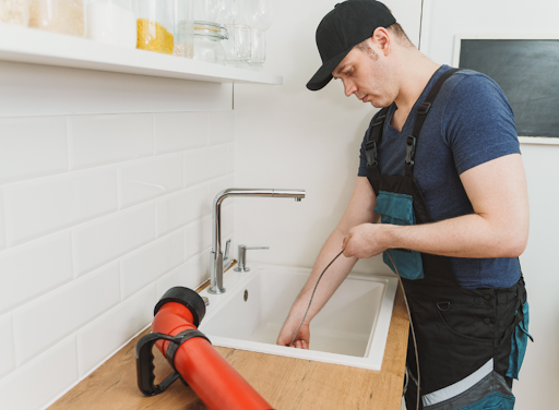 Residential plumber using equipment to clear a clogged kitchen sink drain.