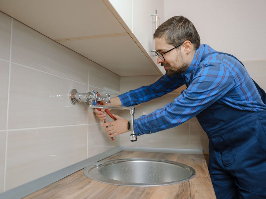 A plumber fixing a dripping faucet to prevent plumbing issues.